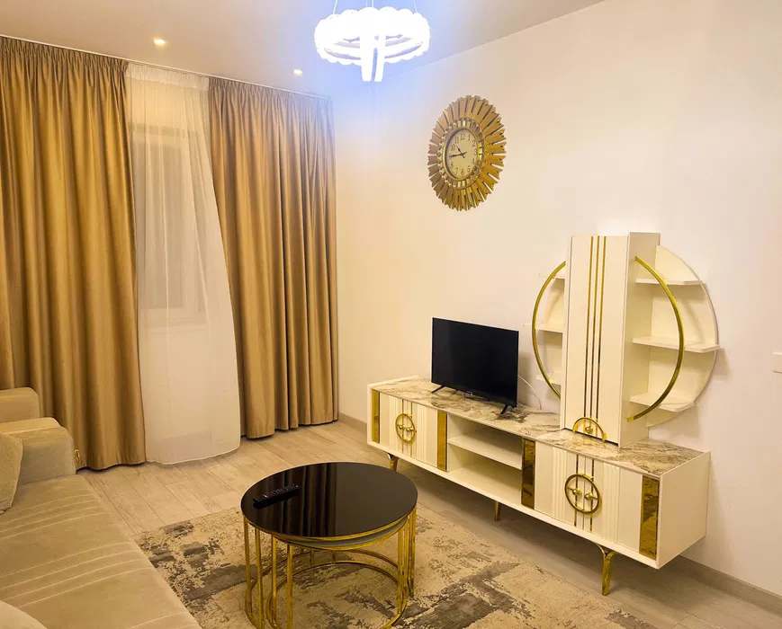 Un soggiorno con una TV a schermo piatto, un tavolo e un orologio — appartamento a Bucuresti